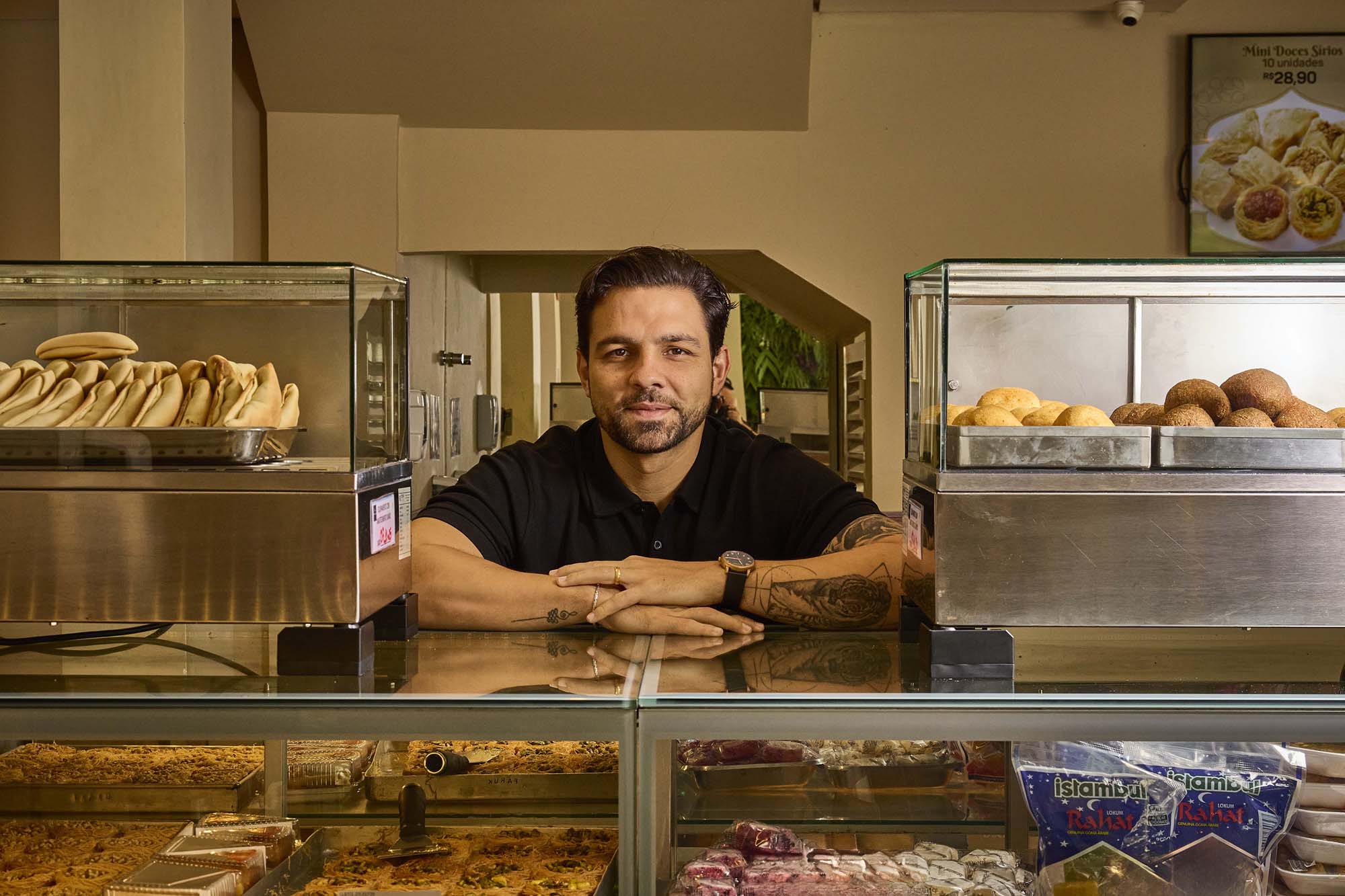 Filipe Mello no balcão do restaurante, cercado por esfihas e doces árabes