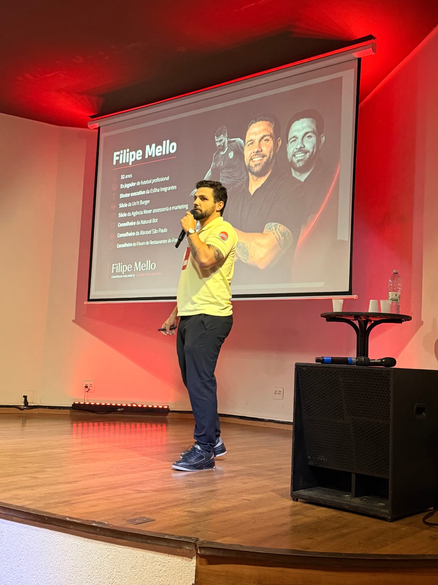 Filipe Mello palestrando em auditório com iluminação vermelha